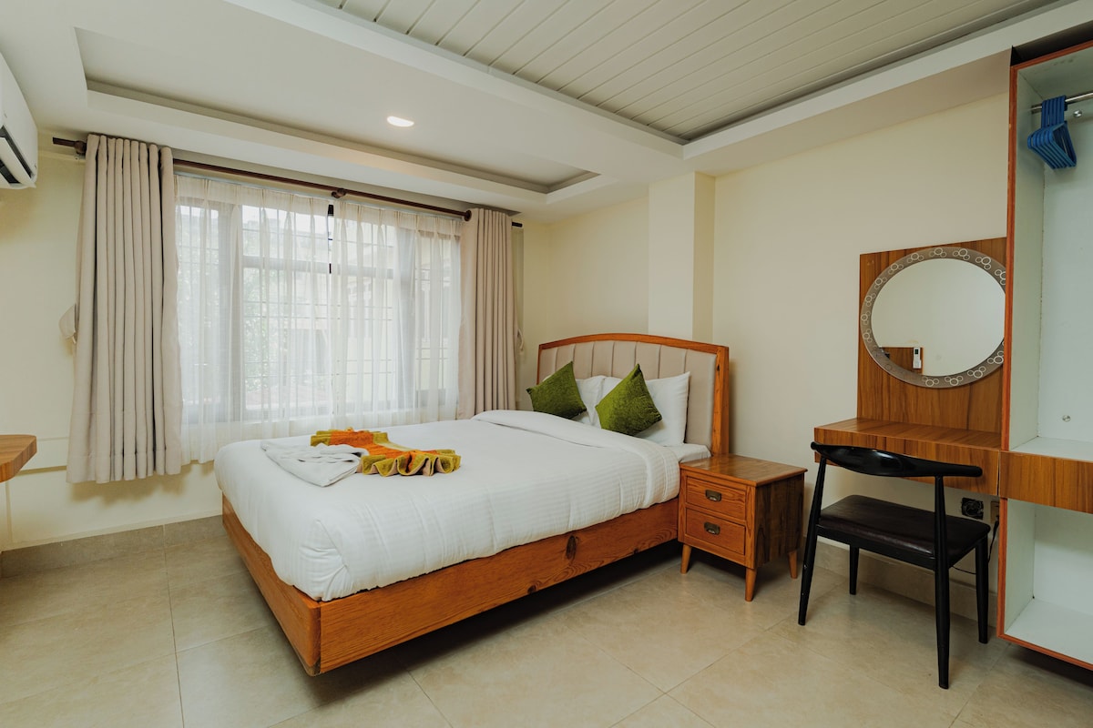 A hotel room with a wooden bed, a nightstand, a chair, a mirror, and a window with curtains.