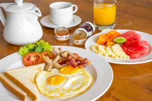 A breakfast setting with a plate of eggs, bacon, mushrooms, and toast, a plate of fruit, a pitcher, cups, and a glass of orange juice. - Mera Peak Hotel (Kathmandu)