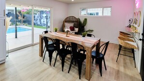 Ein Essbereich mit einem Holztisch und schwarzen Stühlen, eine Glastür zum Pool und eine kleine Pflanze auf dem Tisch.