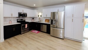 A modern kitchen with white cabinetry, stainless steel appliances, and a wooden floor.