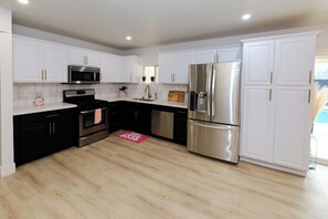 A modern kitchen with white cabinetry, stainless steel appliances, and a wooden floor.