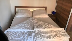 A bed with white bedding, a wooden headboard, and a nightstand with a blue object. - Apartment '3-Wangerooge' with Wi-Fi (Dornum)
