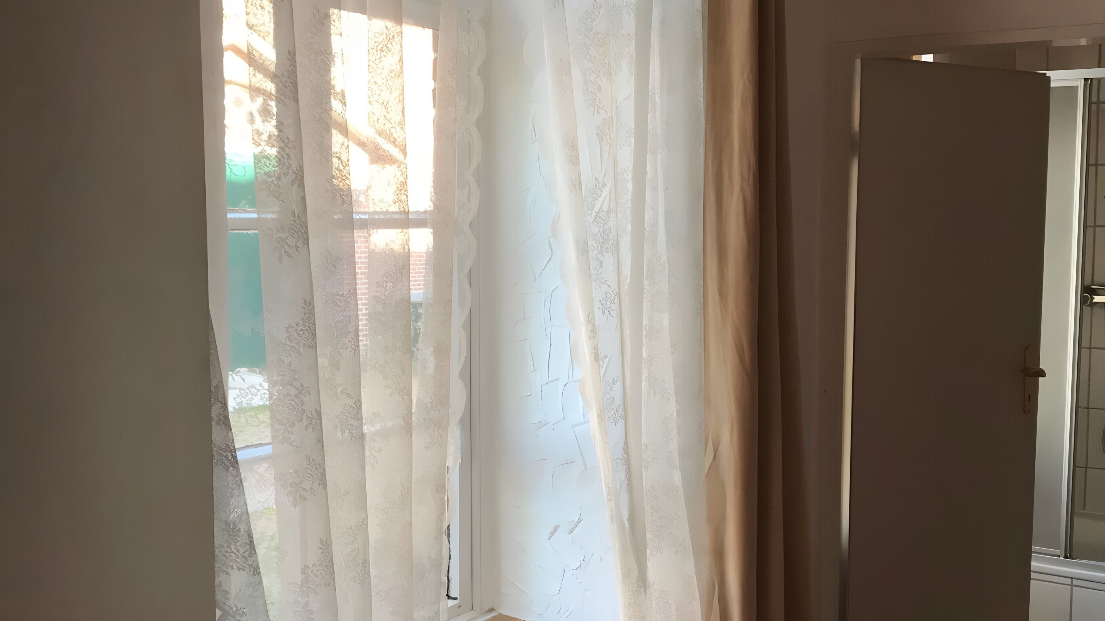 A room with a partially open door and a window with sheer curtains.