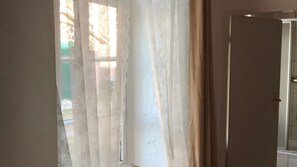 Une pièce avec une porte entrouverte et une fenêtre ornée de rideaux légers.