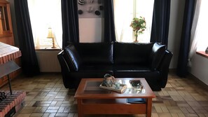 A living room with a black leather sofa, a wooden coffee table, and a potted plant. - Apartment '3-Wangerooge' with Wi-Fi (Dornum)
