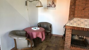 Una habitación de esquina con chimenea de ladrillo, dos sillones de cuero, una mesa con mantel rojo y una lámpara de pared.