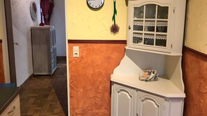 Käytävässä on seinäkello, patteri, koriin varustettu kaappi ja lasipaneelilla varustettu ovi.