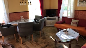 A living room with a sofa, a dining table, chairs, a television, and a glass table with a cloth. - Holiday Apartment '4-Juist' with Wi-Fi (Dornum)
