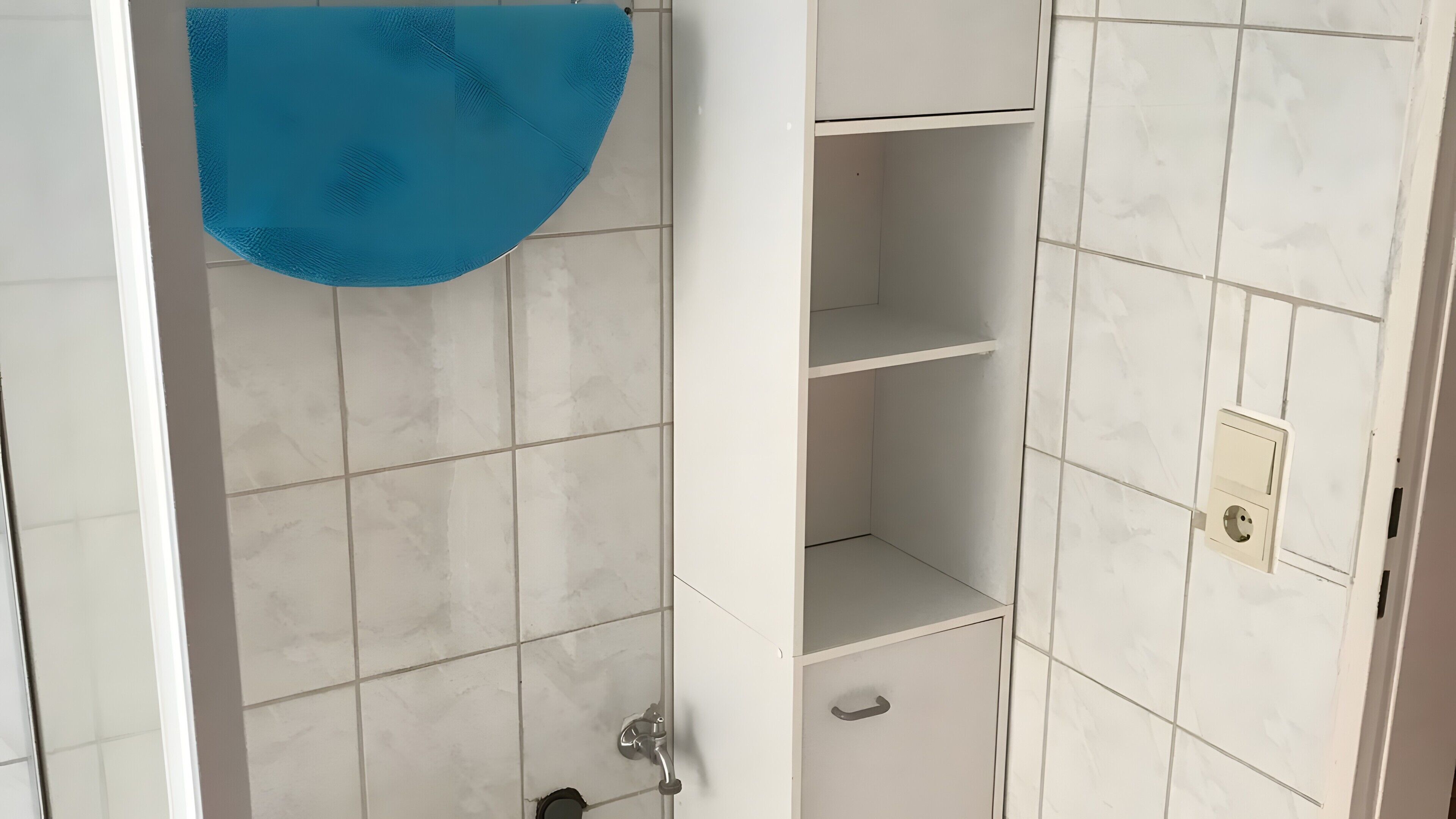 A bathroom with white tiles, a blue towel, and a shower area.