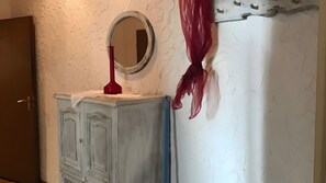 A room with a white textured wall, a wooden door, a white cabinet with a mirror, and a red object on top. - Holiday Apartment '4-Juist' with Wi-Fi (Dornum)