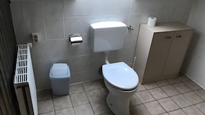 A bathroom with a toilet, a trash bin, a cabinet, and a paper towel dispenser. - Holiday Apartment "Spiekeroog" – 1 Bedroom (Dornum)