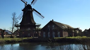 A traditional windmill, a river, and a row of houses with a clear sky. - Holiday Apartment "Spiekeroog" – 1 Bedroom (Dornum)