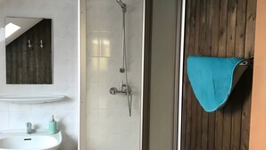 A bathroom with a shower, sink, and wooden panel wall. - Holiday Apartment "Spiekeroog" – 1 Bedroom (Dornum)