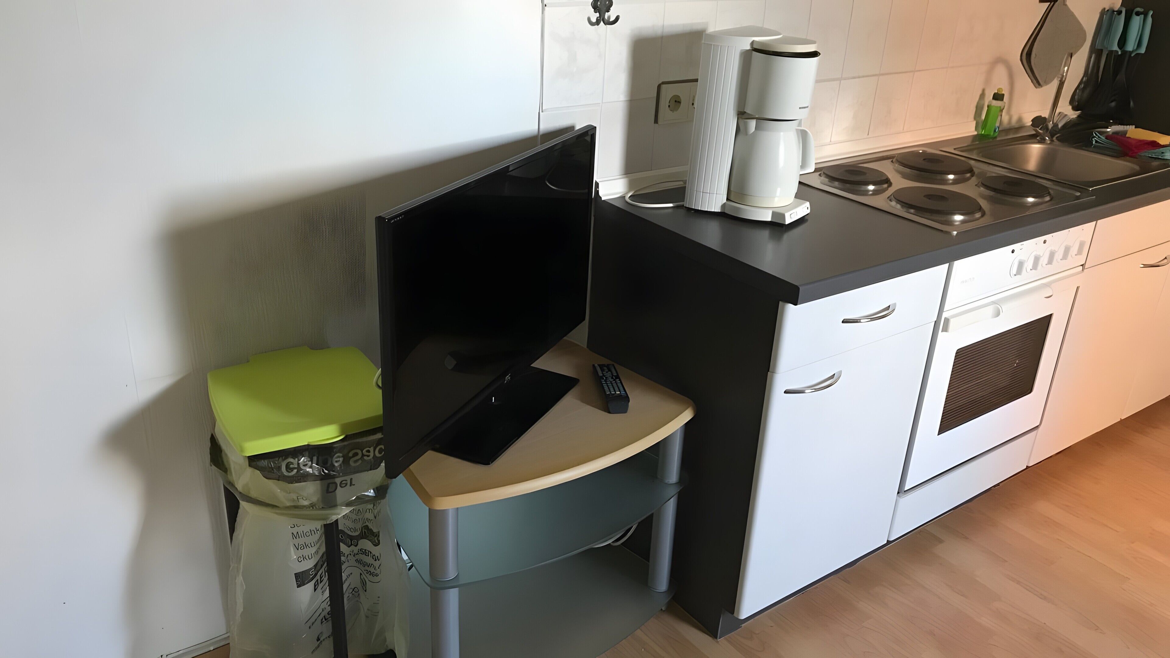 Una cocina compacta con horno integrado, cafetera y un taburete pequeño.
