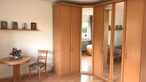 Ein Zimmer mit einem Holzschrank, einem kleinen runden Tisch mit Stuhl und einer Blumenvase.