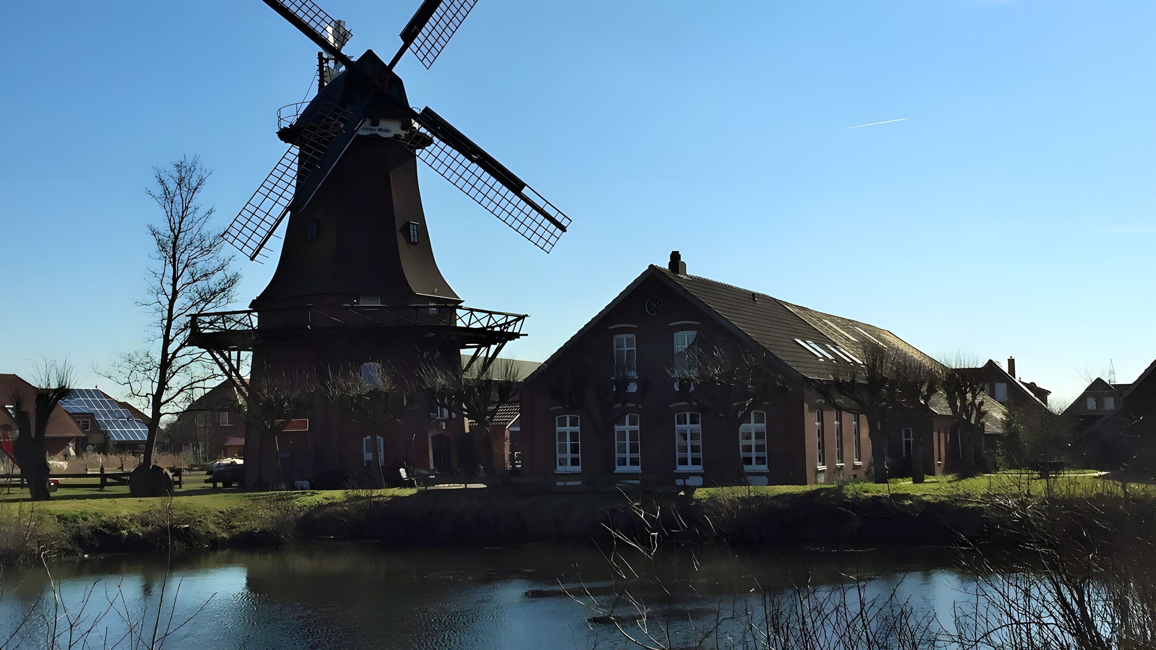 Un moulin à vent traditionnel, une rivière et une rangée de maisons, le tout sous un ciel dégagé.