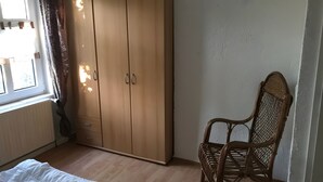 Ett rum med en garderob, en flätad stol och ett fönster med gardiner.