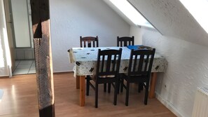A dining area with a table covered by a patterned tablecloth, four wooden chairs, and a skylight above. - Apartment "Baltrum" – 1 Bedroom (Dornum)