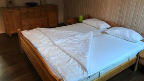 Ein Bett mit Holzbettgestell und weißer Bettwäsche, ein Holzschrank und ein grüner Eimer in einem Zimmer mit Holzwänden.