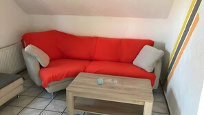 A room with a red sofa, a small wooden table, and a radiator. - Apartment Borkum – 3 Bedrooms (Dornum)