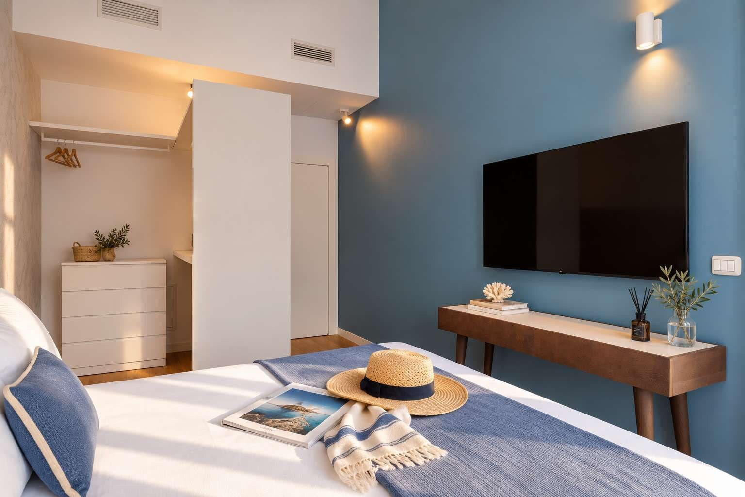 Ein modernes Schlafzimmer mit einem Bett, einem Nachttisch, einem an der Wand befestigten Fernseher und einem Kleiderschrank.