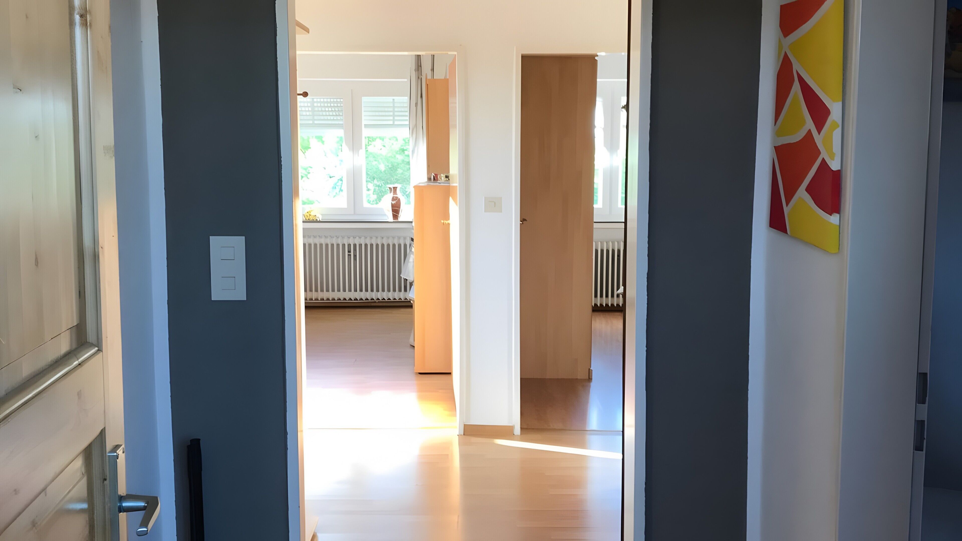 A hallway leading to a room with a radiator, a window, and a door with a light switch.