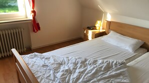 En snyggt bäddad säng med vita sängkläder i ett rum med en sänggavel i trä, en sänglampa och ett fönster med gardiner.