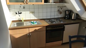 Cocina compacta con pileta, estufa y horno, alacenas de madera y una ventana sobre la encimera.