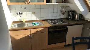 Eine kleine Küche mit Spüle, Herd und Backofen, Holzschränken und einem Fenster über der Arbeitsfläche.