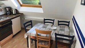 Eine kleine Küche mit Herd, Kaffeemaschine und Wasserkocher, einem Tisch mit Stühlen und einem Fenster über der Spüle.