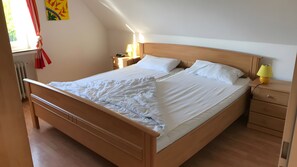 Ein Zimmer mit einem Einzelbett, einem hölzernen Bettgestell, einem Nachttisch mit Lampe und einem Fenster mit Vorhängen.