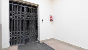 Una habitación con una puerta con barrotes, un extintor de incendios sujeto a la pared y una alfombra pequeña en el suelo.