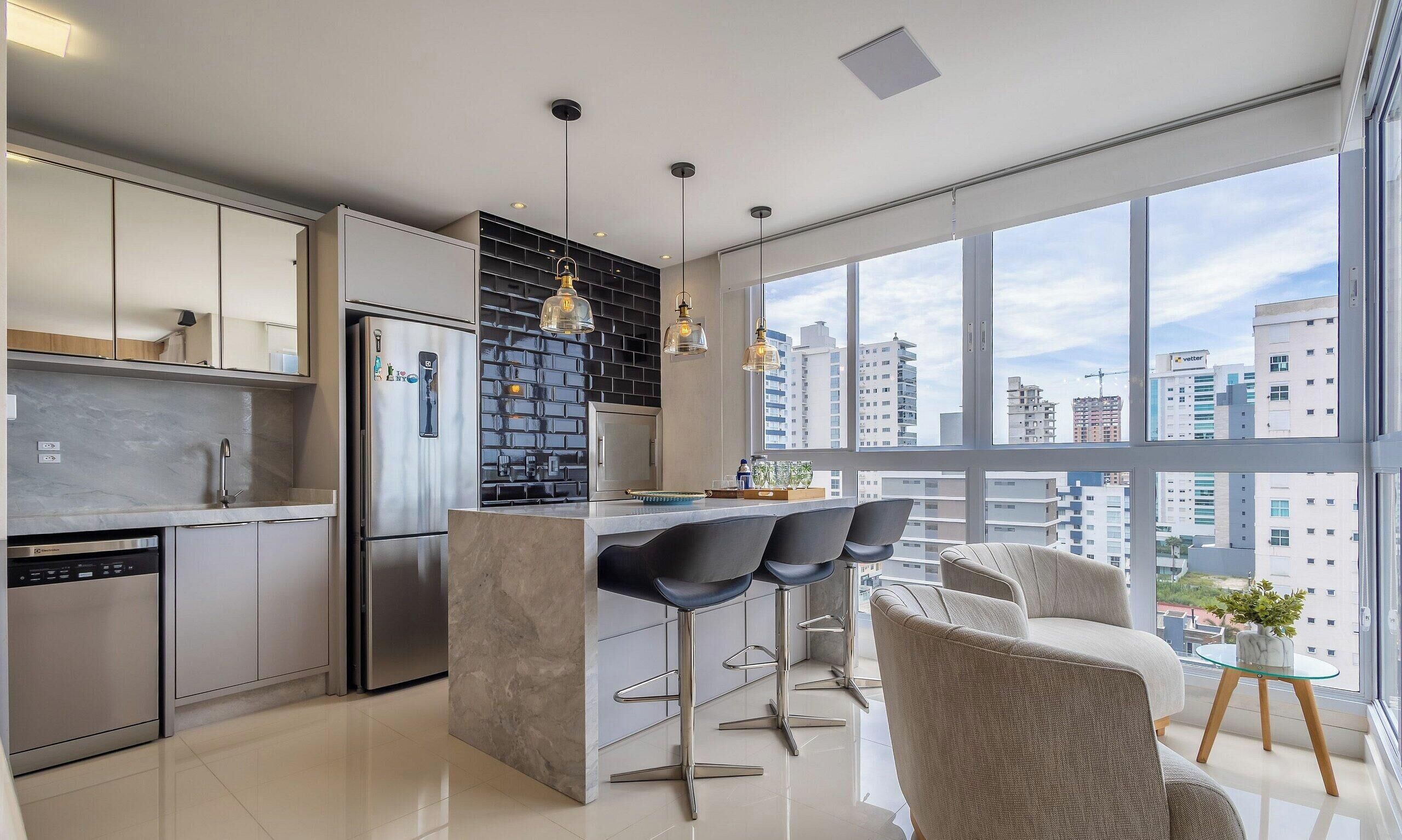 A modern kitchen with a central island, bar stools, and a view of the city through large windows.