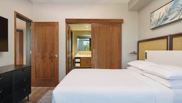 Um quarto com cama, cômoda, espelho e porta para um banheiro.
