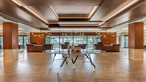 Um hall amplo com uma mesa de vidro central, balcões de recepção em madeira e um design de teto moderno.