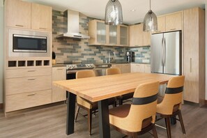 Una cocina moderna con armarios de madera, un refrigerador de acero inoxidable, un microondas y un comedor con sillas de mimbre.