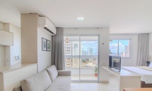A modern living room with a sofa, a flat-screen TV, and a balcony with a city view. - Studio w/ in Setor Bueno - Lhd2007 (Goiânia)