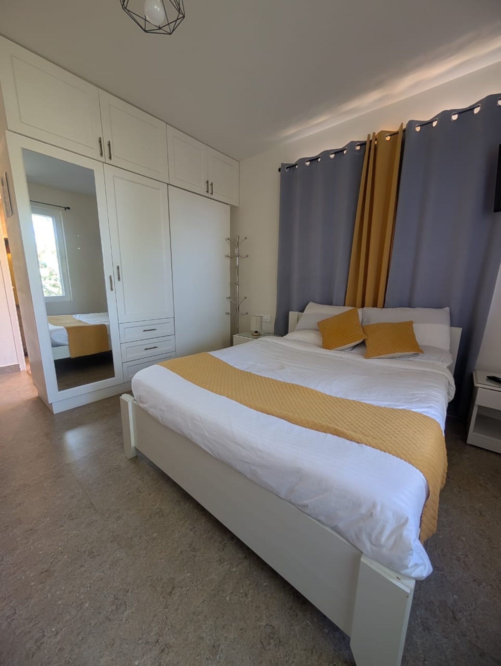 A bedroom with a bed, a wardrobe, a mirror, and a nightstand.