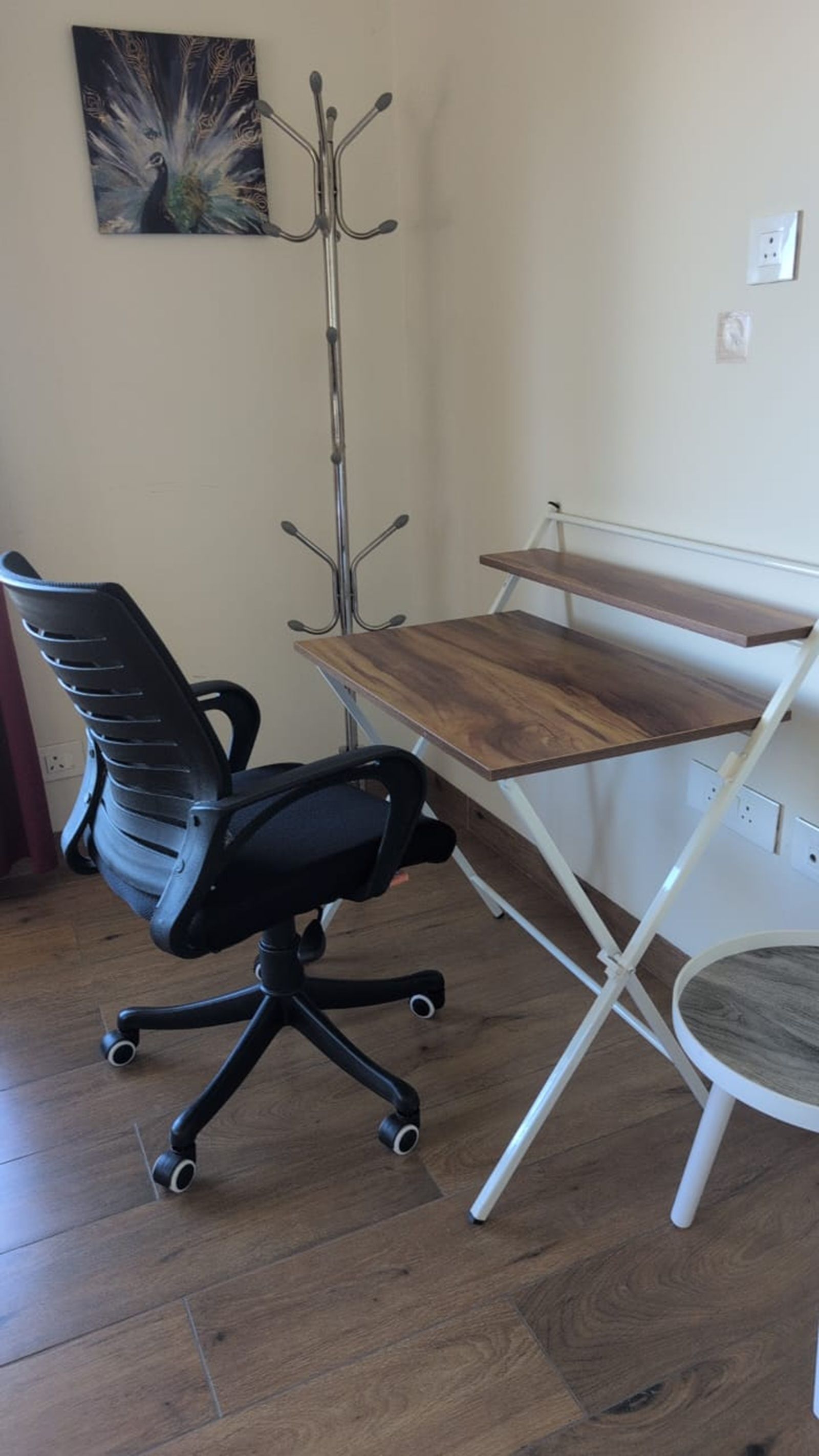Un espace de travail comprenant un bureau en bois, un fauteuil de bureau noir et un porte-manteau.