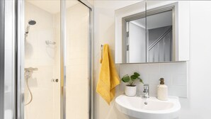 A bathroom with a glass shower enclosure, a white sink, a mirror above the sink, and a yellow towel hanging on the wall. - Student Only Causeway View (Aberdeen)