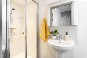 A bathroom with a glass shower enclosure, a white sink, a mirror above the sink, and a yellow towel hanging on the wall. - Student Only Causeway View (Aberdeen)
