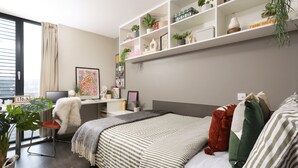 A modern bedroom with a bed, a desk, a chair, and a shelving unit with plants. - Student Only Causeway View (Aberdeen)