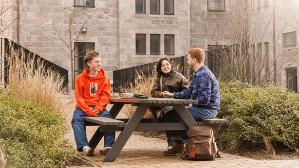 Three individuals seated at a picnic table outdoors with a stone building in the background. - Student Only Causeway View (Aberdeen)