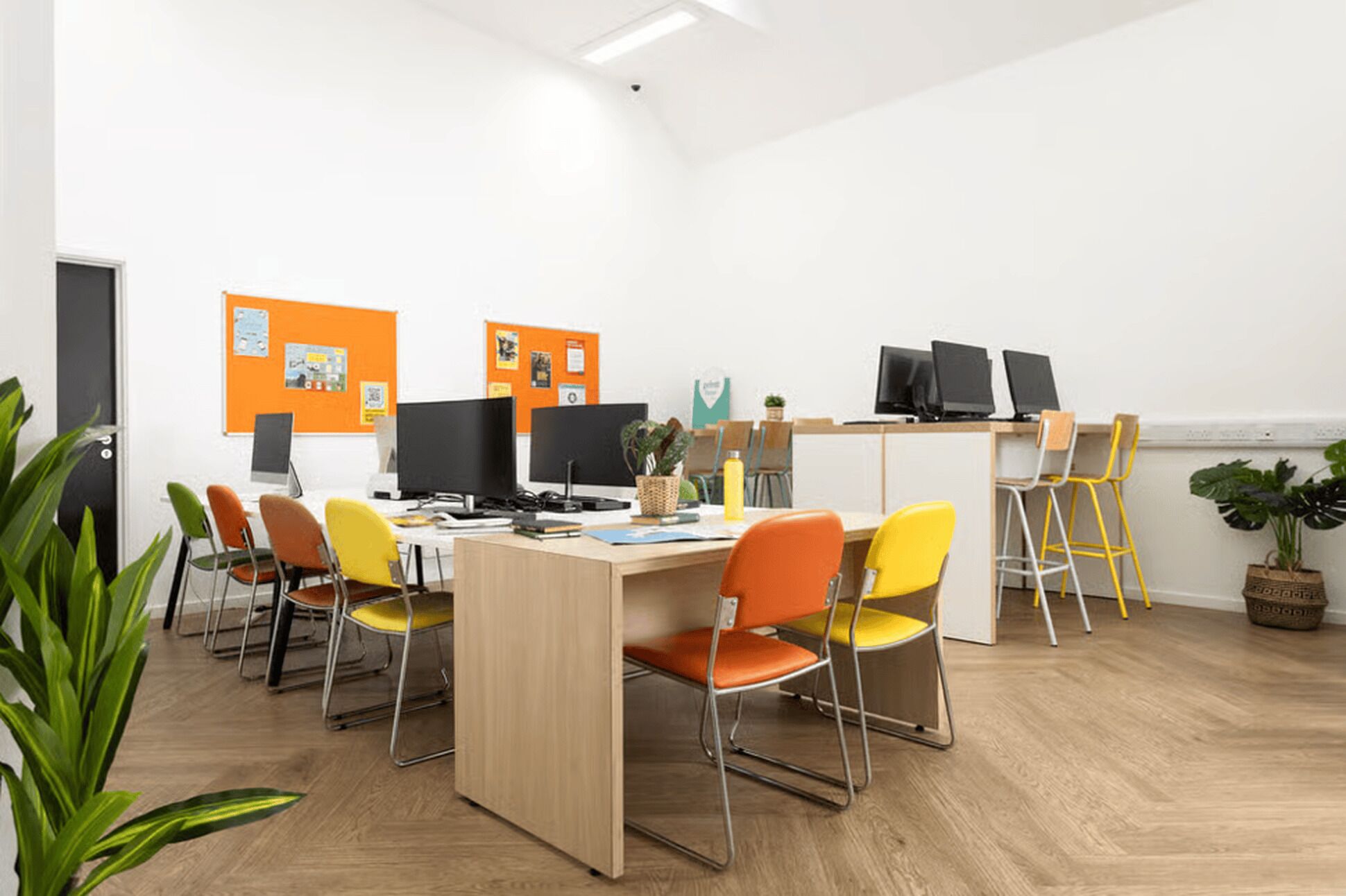 Un espace de bureau moderne avec une grande table, plusieurs chaises et des ordinateurs.