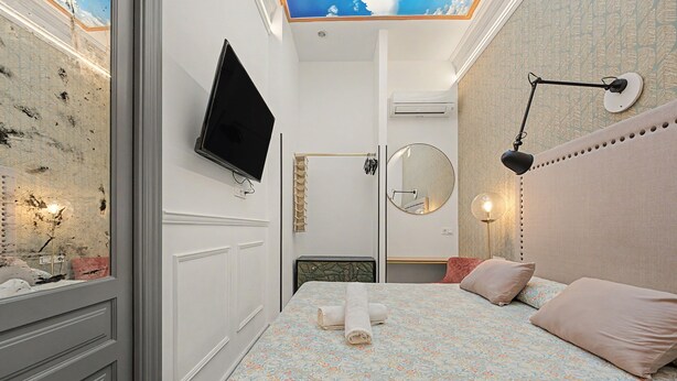 Un dormitorio con cama, televisión, espejo y techo con tragaluz.