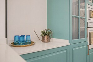 A kitchen counter with a tray holding blue glasses, a potted plant, and a white cabinet with a window. - El Mar Azul 1 Beachfront Apartment, Wi-Fi, Air Conditioning (Torremolinos)
