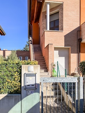 A residential building with a brick facade, a set of stairs leading to a garage, and a gated entrance.