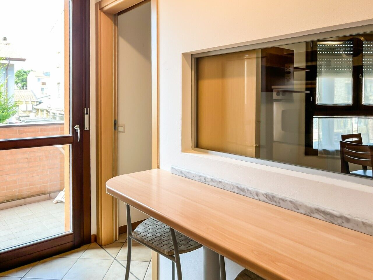 Ein Zimmer mit Holztisch und -stühlen, einer Schiebeglasdoor und Blick ins Freie.