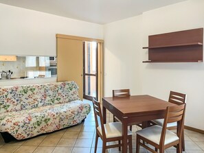 A living room with a sofa and a dining table with chairs. There is a kitchen area with cabinets and a microwave.