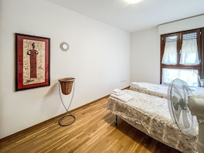 A room with two beds, a standing fan, a framed artwork, and a small decorative item on the wall.